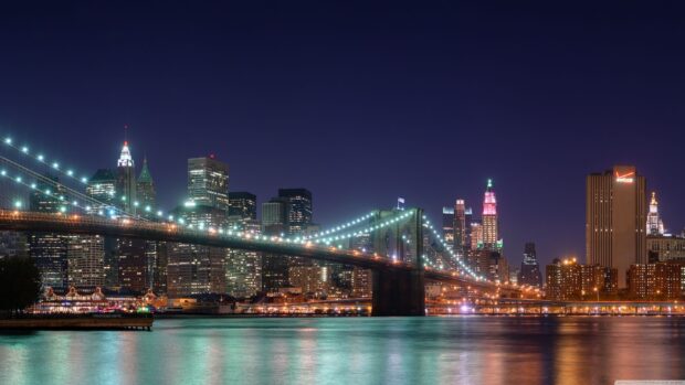 A beautiful view of New York skyline showing the Brooklyn Bridge at night with city lights reflecting on the water