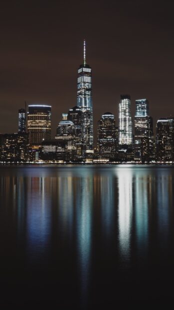 The New York skyline at night with illuminated buildings reflecting on the water surface