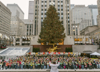 A large group of musicians performing in front of the New York Christmas tree at Rockefeller Center