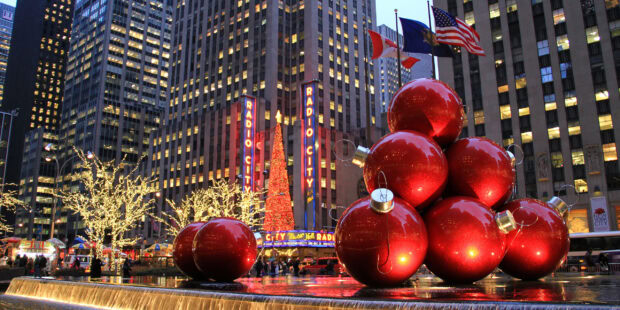 Large red Christmas ornaments stacked near Radio City in New York Christmas scene at dusk