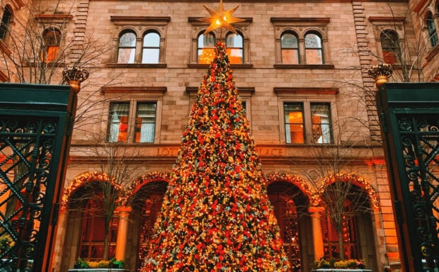 A decorated Christmas tree with lights and ornaments in front of a New York building during Christmas