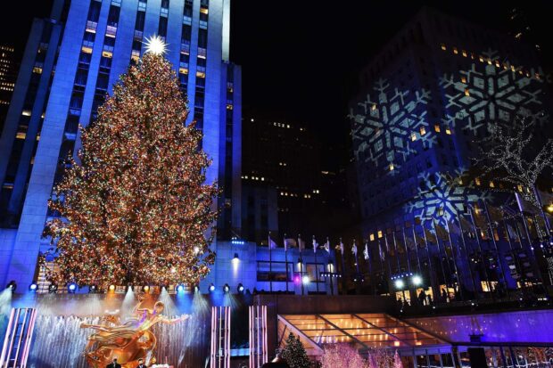 New York Christmas tree decorated with colorful lights in front of buildings with snowflake projections at night