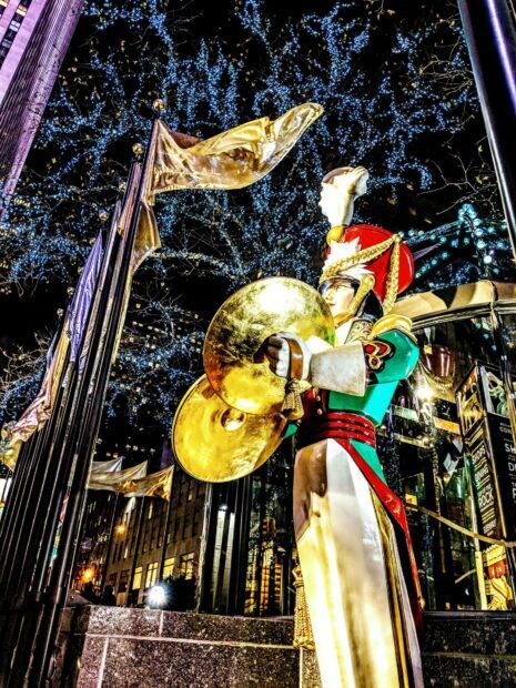 A drummer figurine with cymbals stands in front of illuminated trees in New York Christmas decorations