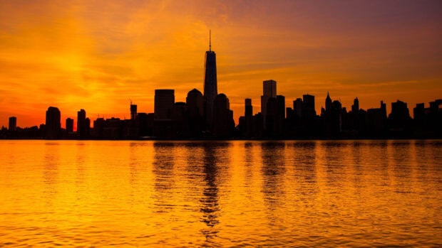 New York skyline silhouette at sunset with golden sky and water reflection