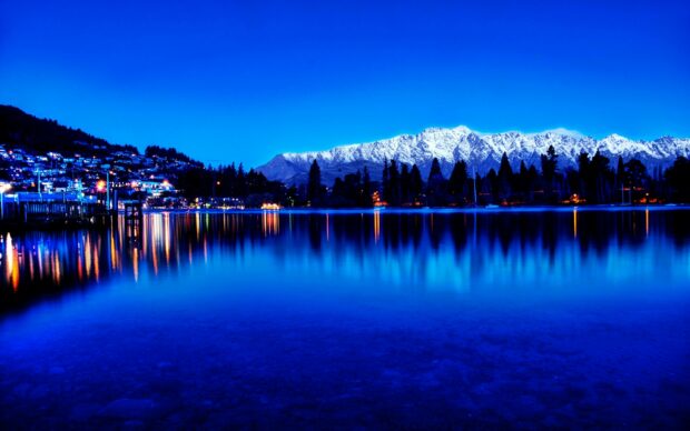 Snow capped mountains and city lights reflecting on the lake in New Zealand