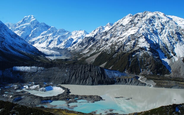 Snow covered mountains surround a turquoise glacial lake in a New Zealand alpine valley