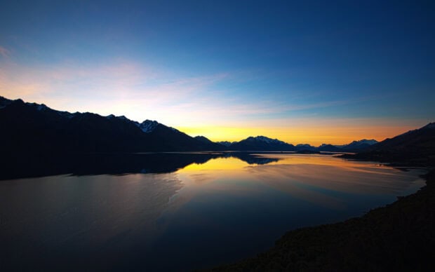 Stunning New Zealand mountain range reflecting on lake water at sunset with colorful sky