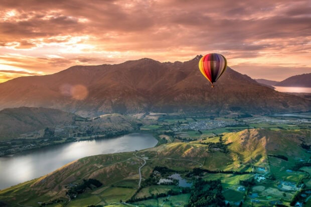 A scenic view of New Zealand mountains and lakes with a hot air balloon floating at sunset