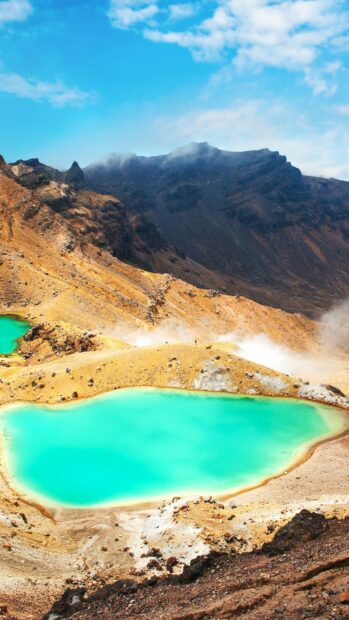 A volcanic crater with turquoise water in New Zealand surrounded by rocky terrain and mountains
