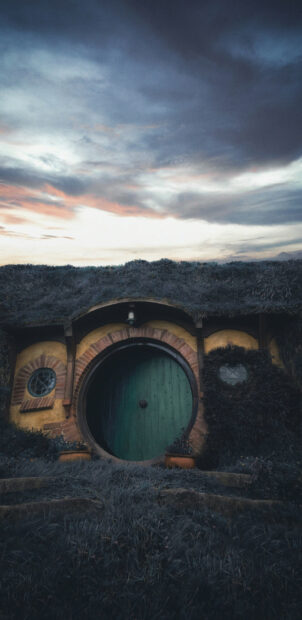 A Hobbit house with a green round door surrounded by grass in New Zealand