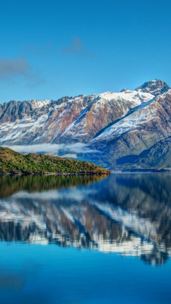 Snow capped mountains in New Zealand reflected on calm lake water with clear blue sky