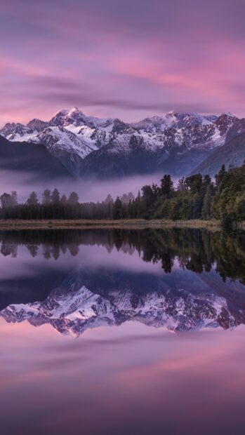 Snowy mountain range in New Zealand reflected in calm lake at dawn with purple sky