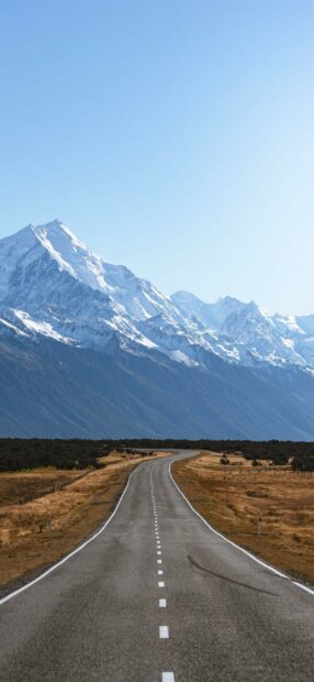 A winding road leading towards towering snow capped mountains in New Zealand landscape