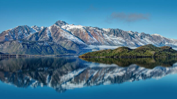 Snow capped mountain range in New Zealand reflects clearly in the calm lake water