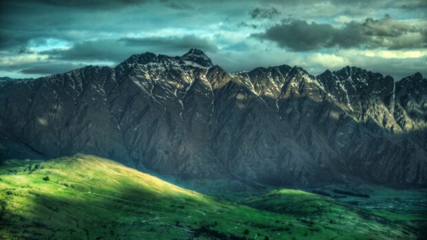 Rugged New Zealand mountain range with green hills under dramatic cloudy sky