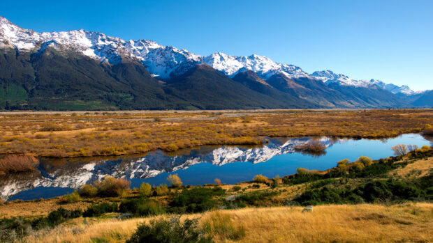 Snow capped mountains in New Zealand with river reflection and autumn vegetation in foreground