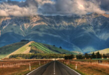 A scenic New Zealand landscape featuring mountains and a road leading towards them under cloudy skies