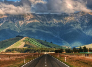A scenic New Zealand landscape featuring mountains and a road leading towards them under cloudy skies