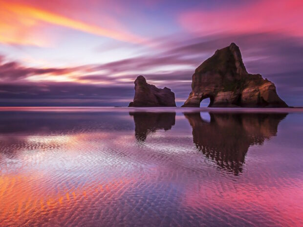 Natural rock formations in New Zealand coastline during vibrant sunset