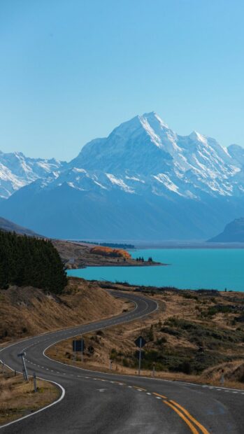 A winding road leading to snow covered mountains with a turquoise lake in New Zealand