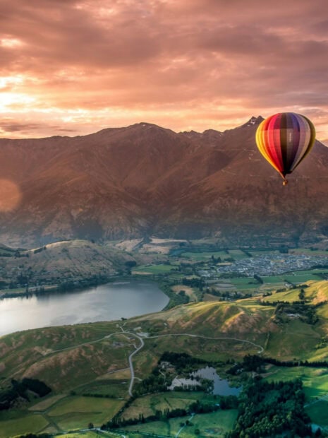 Hot air balloon flying over New Zealand scenic landscape with mountains and lakes at sunset