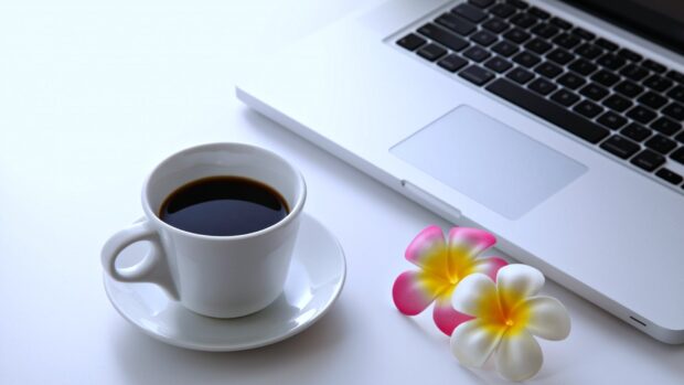 A cup of black coffee and colorful flowers beside a notebook on a white surface