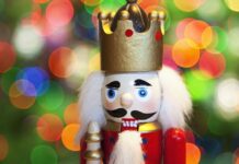 A close up of a nutcracker figure with a golden crown and white hair against colorful blurred lights background