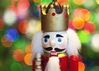 A close up of a nutcracker figure with a golden crown and white hair against colorful blurred lights background