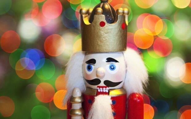 A close up of a nutcracker figure with a golden crown and white hair against colorful blurred lights background