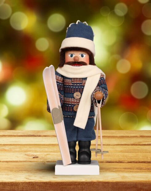 A nutcracker figure dressed for winter holding skis and ski poles standing on a wooden surface