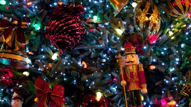 A colorful nutcracker figure standing on a decorated Christmas tree with bright lights and ornaments
