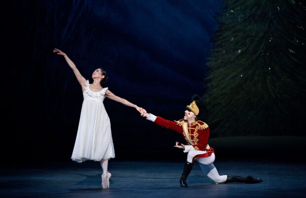 A dancer wearing a red uniform and a ballerina in a white dress perform a Nutcracker scene on stage