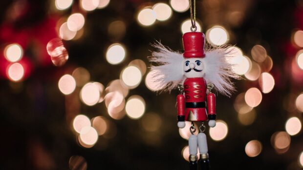 A detailed nutcracker with white hair and red uniform hanging against blurred lights background