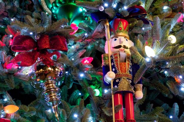 A festive nutcracker figure standing on a decorated Christmas tree with colorful lights and ornaments