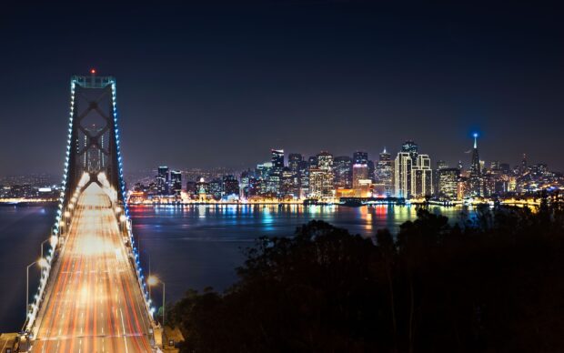Nighttime cityscape featuring Oakland skyline and bridge lights reflecting on water