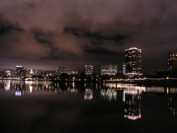 Nighttime cityscape with Oakland skyline reflecting on calm water under cloudy sky