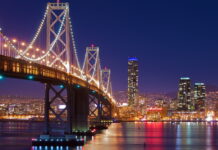 Night view of Oakland skyline with illuminated bridge and city lights reflecting on water (1)