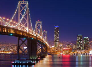 Night view of Oakland skyline with illuminated bridge and city lights reflecting on water (1)