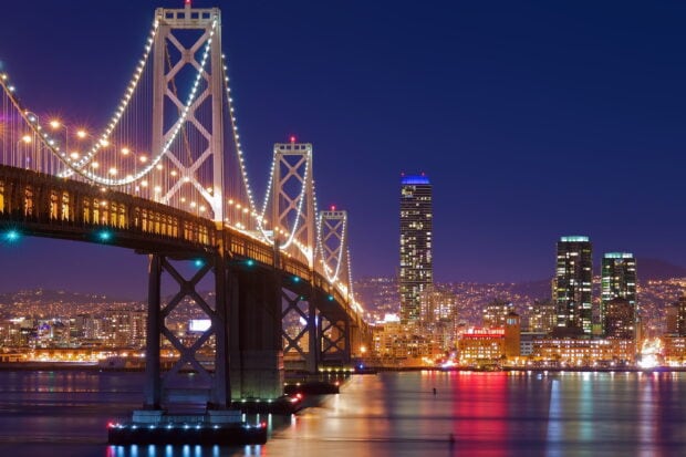 Night view of Oakland skyline with illuminated bridge and city lights reflecting on water (1)