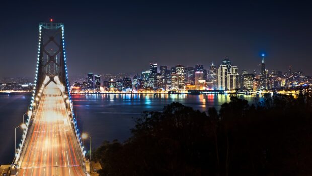 Night view of Oakland skyline with illuminated bridge and city lights reflecting on water