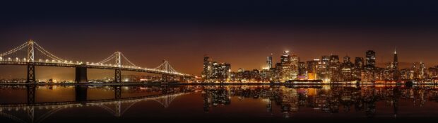 Nighttime view of Oakland skyline with illuminated buildings and bridge reflected in water