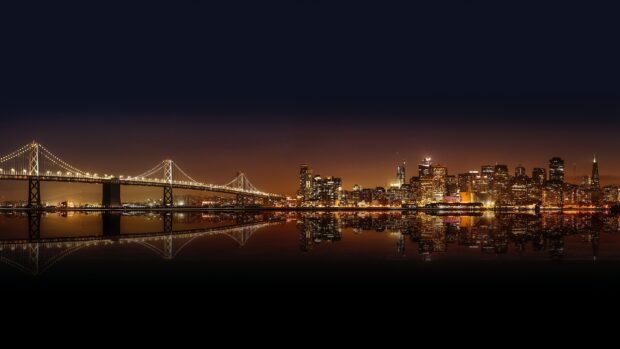 Oakland skyline at night with illuminated buildings and bridge reflections across the water