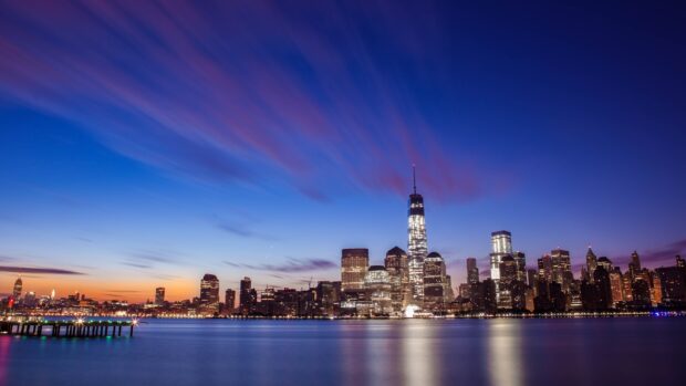 The cityscape of Oakland skyline at dusk with illuminated buildings and vibrant sky purple hues