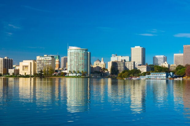 The Oakland skyline reflects beautifully on the calm water under a clear blue sky