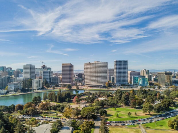 A panoramic view of Oakland skyline featuring tall buildings and a park with a lake under a blue sky