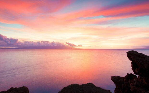Calm ocean landscape with colorful sunset sky and rocky shore in the distance