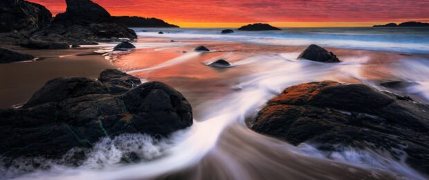 Rocky ocean landscape with sunset sky and flowing water on the beach