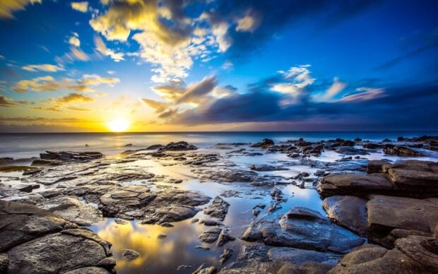 Rocky ocean landscape with vibrant sunset and dramatic sky clouds reflecting on water pools