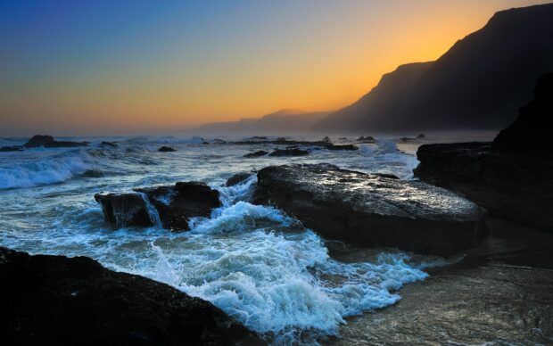 Rocky ocean landscape with waves crashing at sunset near cliffs