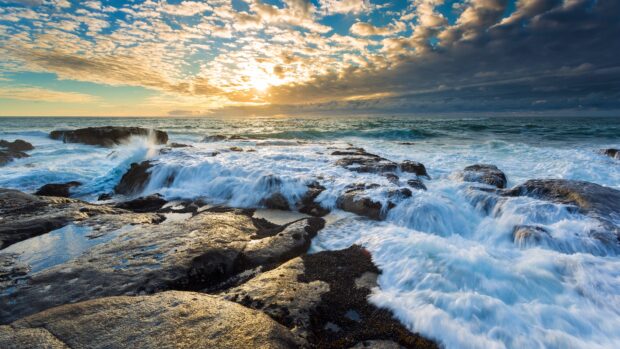 Ocean landscape with crashing waves over rocky shore during sunset